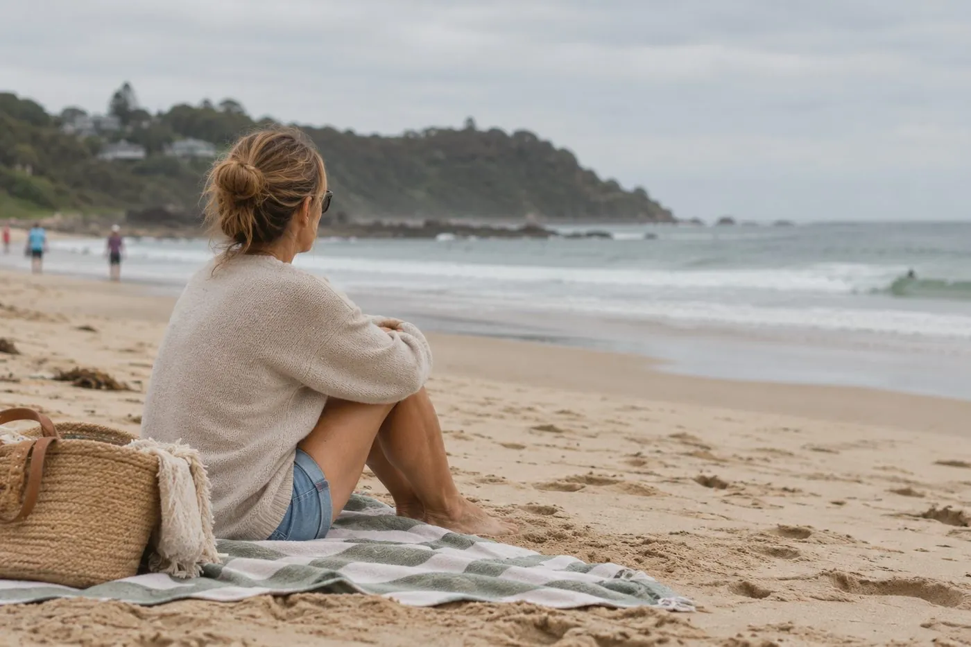 A woman sitting on the sand looking out to sea